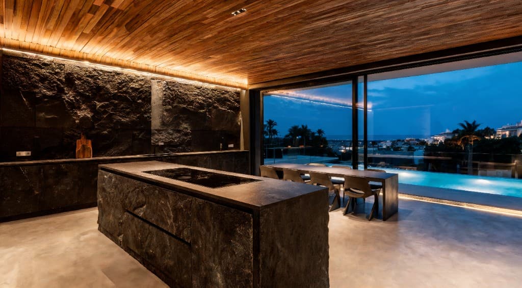 Luxury kitchen and dining room with stone island and pool view at dusk